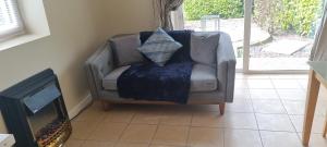 Pinewood Lodge في كورك: كرسي رمادي مع بطانية زرقاء يجلس بجوار موقد