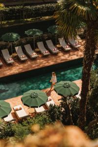 - une femme qui se promène au bord d'une piscine avec des chaises et des parasols dans l'établissement Parkhotel Mondschein, a Member of Design Hotels, à Bolzano