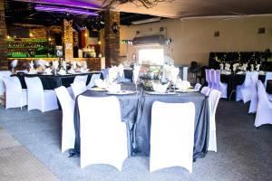 una fila de mesas con sillas blancas en una habitación en Buffalo’s Backpackers and Party Venue, en Cullinan