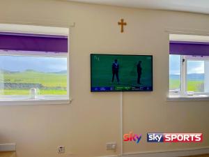 a flat screen tv on a wall with two windows at Kilchrist Castle Cottages in Campbeltown