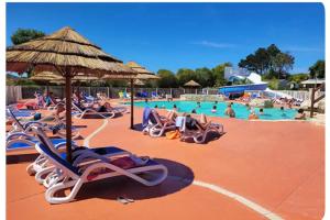 a pool with people laying in chairs and an umbrella at Mobile-home Camping 4 etoiles bord de mer in Ouistreham