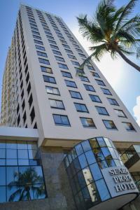 a tall building with a palm tree in front of it at Seara Praia Hotel in Fortaleza