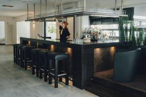 een vrouw achter een bar met zwarte krukken bij nordica Hotel Friesenhof in Büsum