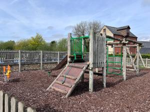 a playground with a slide in front of a fence at Kingfisher House in Somerford Keynes