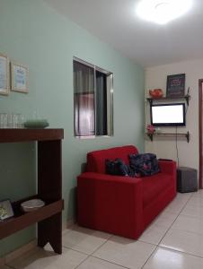 um sofá vermelho numa sala de estar com uma televisão em Apt. de Setiba - HOSPEDARIA OCA RUCA em Guarapari