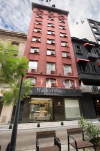 un edificio alto de color rojo con un banco delante de él en Hotel Waldorf en Buenos Aires