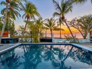 a swimming pool with palm trees and a sunset at Kay Alice - Beachfront Villa in Le Carbet