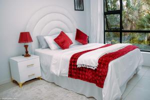 a bedroom with a white bed with red pillows and a window at Casa de Amor - Stylish Apartment in Rosebank in Johannesburg