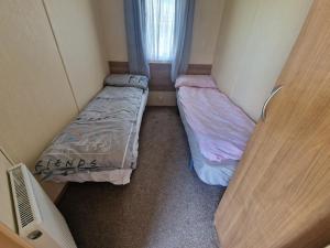 2 camas en una habitación pequeña con ventana en B17 Sunnymede Caravan Park, Fantasy Island, Ingoldmells, en Ingoldmells