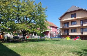 a park in front of a building with a tree and a playground at Apartmanii Gajić in Kuršumlija