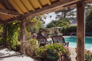 uma pérgola de madeira com cadeiras e flores ao lado de uma piscina em 7 Bedrooms Manor Farmhouse with heated pool em Cirencester