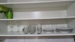 una estantería blanca con copas, platos y copas de vino en Kitnet en Caxias do Sul