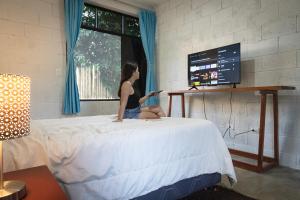 Eine Frau, die auf einem Bett vor einem Fernseher sitzt. in der Unterkunft La Casa de Marlon y Karina in Tarapoto