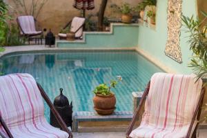 Zwei Stühle und eine Topfpflanze stehen neben einem Schwimmbecken. in der Unterkunft Riad Norma in Fès
