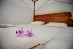 zwei lila Blumen auf einem weißen Bett in der Unterkunft Serene Home Stay in Udawalawe
