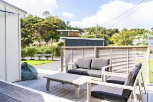 a patio with a couch and a chair on a deck at Pearl's Embrace - Mangawhai Heads Studio in Mangawhai