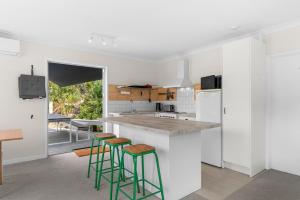 a kitchen with white walls and green bar stools at Pearl's Embrace - Mangawhai Heads Studio in Mangawhai