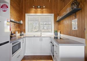 cocina con armarios blancos, fregadero y ventana en North Lodge Highland Cottage, en Pokolbin