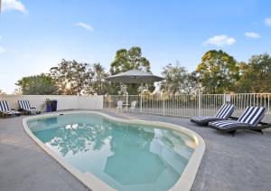 a swimming pool with lounge chairs and an umbrella at North Lodge Highland Cottage in Pokolbin
