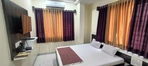 Habitación con cama, TV y cortinas. en Hotel Sai viraj palace, en Shirdi
