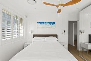 um quarto branco com uma cama e uma ventoinha de tecto em Stunning 2-Bed Coastal Pad Across From the Beach em Sydney