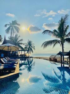 a resort swimming pool with palm trees and the ocean at Sasitara Thai Villas in Choeng Mon Beach