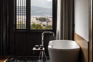 La salle de bains est pourvue d'une baignoire et d'une fenêtre. dans l'établissement 丽江山之名·音糖·大美华宿（束河古镇店）, à Lijiang