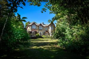 ein altes Haus durch die Bäume an einem sonnigen Tag in der Unterkunft Heatherlie House Hotel in Selkirk