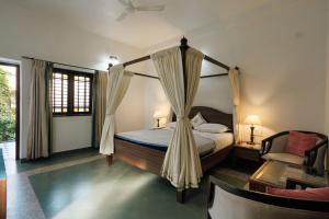 ウドゥピにあるBalkatmane Heritage Spa Resort Udupiのベッドルーム(天蓋付きベッド1台、椅子付)