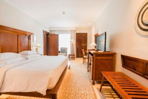 een slaapkamer met een bed, een bureau en een televisie bij Ramayana Suites and Resort in Kuta