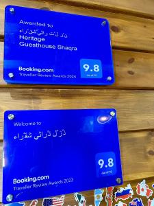 two signs on the wall of a store with a sign for a phone at نُزُل تُراثي شقْراء Heritage Guesthouse Shaqra in Shaqra