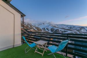 two chairs and a table on a balcony with snow covered mountains at Templo cota 2330m in Sierra Nevada