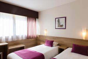 2 bedden in een hotelkamer met paarse kussens bij The Originals City, Le Logis d'Elbée, Cholet Nord (Inter-Hotel) in Beaupréau