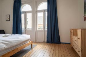 een slaapkamer met een bed en een raam met blauwe gordijnen bij Spacious Belle Epoque House with free parking in Oostende