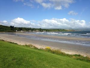 a beach with a green field and the ocean at Stunning Detached 3 Bedroom House Islandandmagee in Larne
