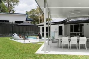 a man and a woman sitting around a pool in a backyard at Amiri on Holbrook - Pet Friendly in Yaroomba
