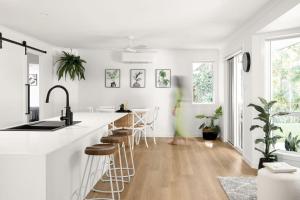 a white kitchen with a counter and stools at Amiri on Holbrook - Pet Friendly in Yaroomba