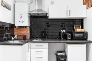 a kitchen with white cabinets and a black brick wall at Whitechapel Grand in London