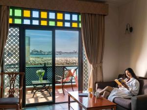 a woman sitting on a couch reading a book in a living room at Novotel Bahrain Al Dana Resort in Manama