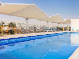 una piscina con sillas, mesas y sombrillas en Novotel Sevilla en Sevilla