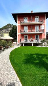 un bâtiment rouge avec une pelouse verte devant lui dans l'établissement Garni Hotello Sport And Relax, à Riva del Garda
