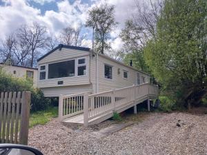 a white tiny house with a porch and a fence at Tree tops - 2 bedroom static caravan with decking in Hastings