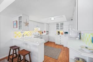 a kitchen with white cabinets and a sink and stools at Ground floor beachfront with steps to the beach and pool & beach access in New Smyrna Beach