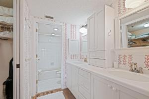 a white bathroom with a sink and a shower at Ground floor beachfront with steps to the beach and pool & beach access in New Smyrna Beach