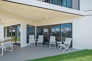 a patio with white chairs and tables and windows at Ground floor beachfront with steps to the beach and pool & beach access in New Smyrna Beach