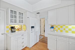 a white kitchen with white cabinets and yellow tiles at Ground floor beachfront with steps to the beach and pool & beach access in New Smyrna Beach