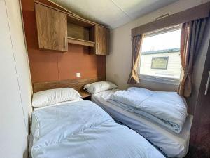 Duas camas num pequeno quarto com uma janela em Lovely 8 Berth Caravan At California Cliffs Nearby Scratby Beach Ref 50060e em Great Yarmouth