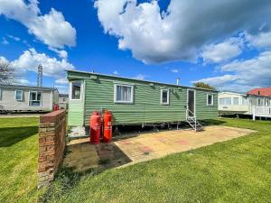 a green tiny house with two red fire hydrants in a yard at Great Caravan At Valley Farm Holiday Park, Essex Ref 46583v in Great Clacton