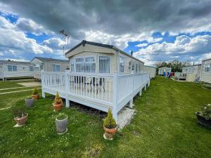 a white house in a yard with potted plants at Gorgeous 6 Berth Caravan With Large Decking Area, Essex Ref 44009f in Great Oakley