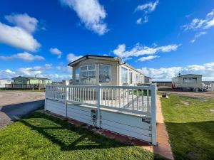 a small house with a white fence in the grass at Ref 40035nd - Superb Caravan With Decking Free Wifi At North Denes Holiday Park in Lowestoft